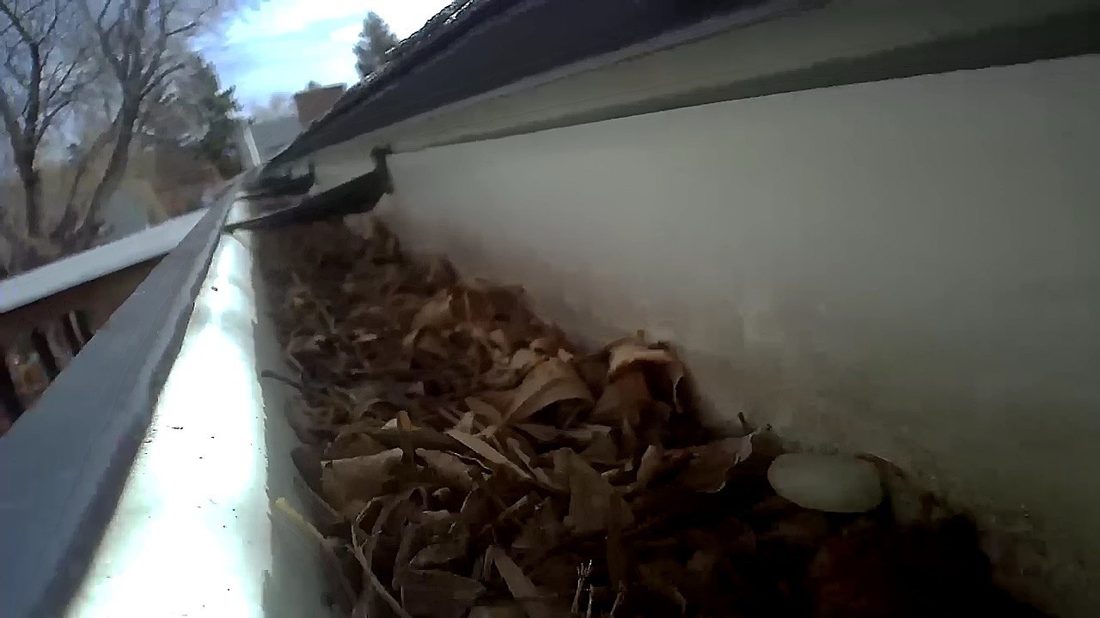 A gutter packed with dry leaves and brush debris along the eaves, the exact ignitable fuel that wind-blown embers land in during a wildfire.